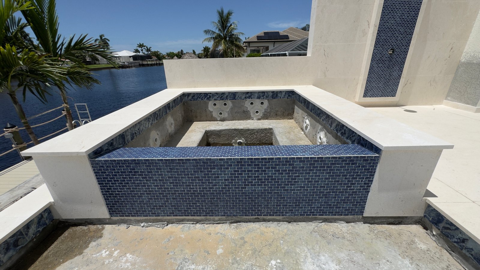 Raised spa with blue glass tile and travertine coping on a waterfront pool
