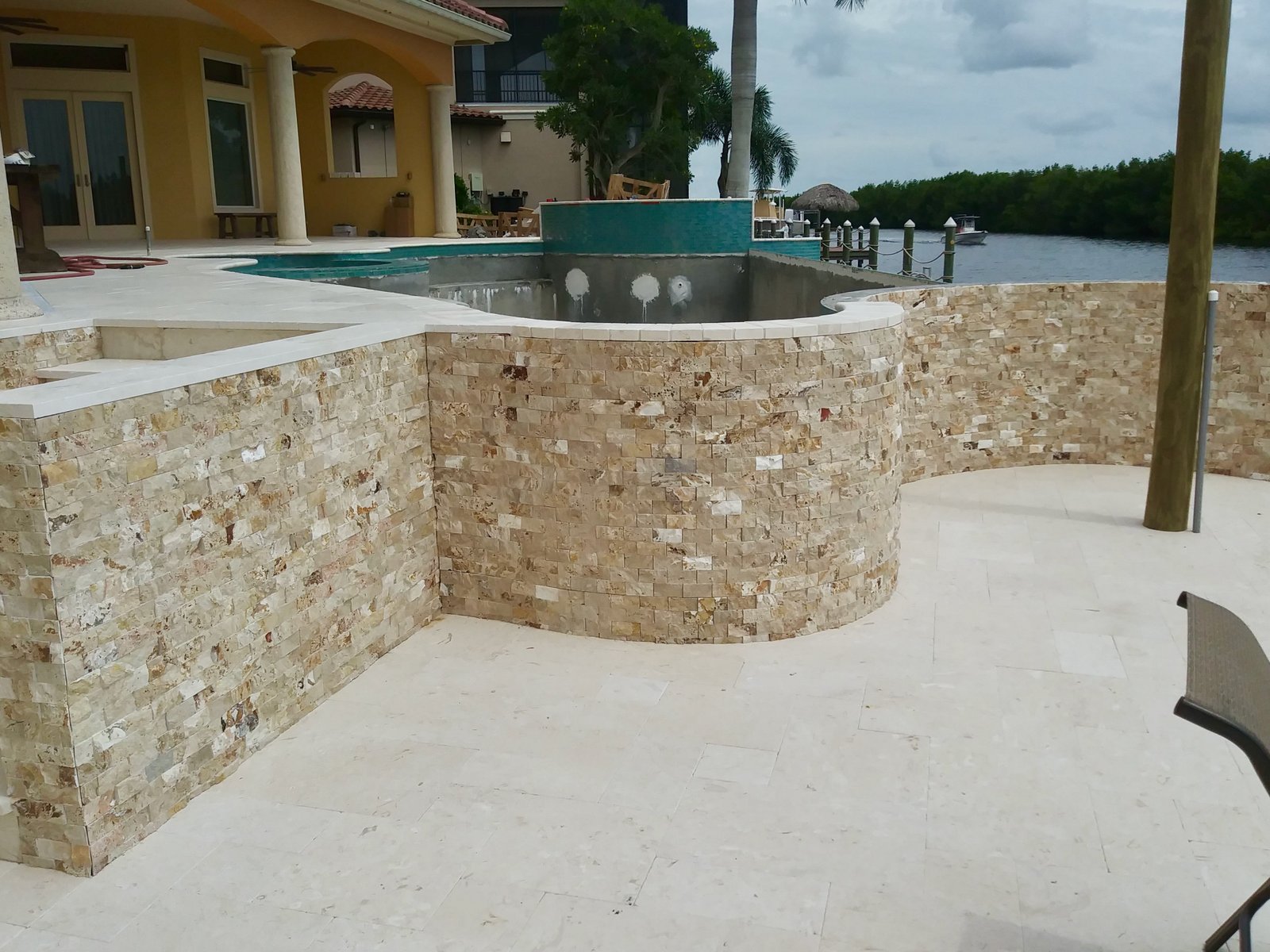 Stone-clad lanai and travertine pool deck on a waterfront property